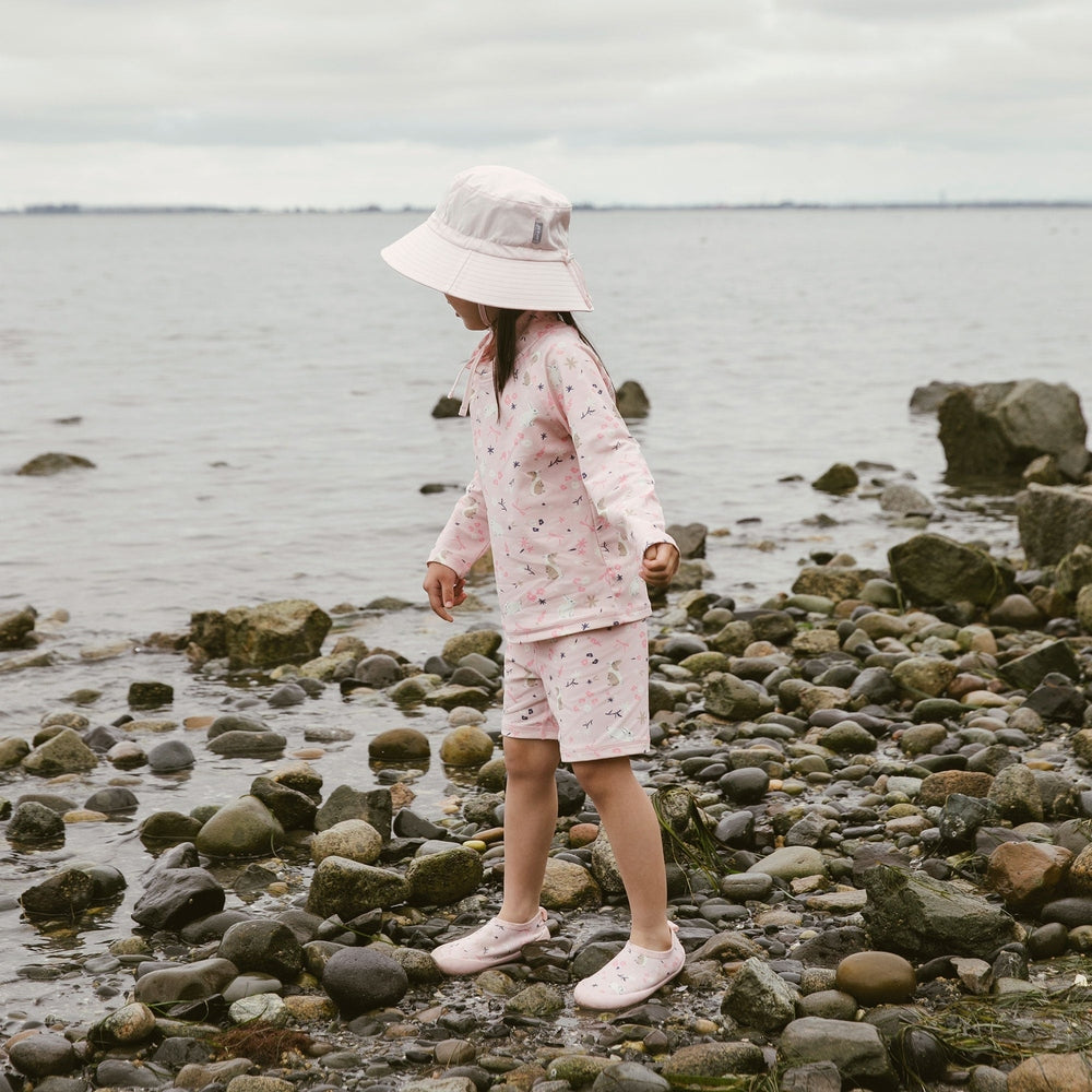 Child in pink beach outfit with sun hat by the water
