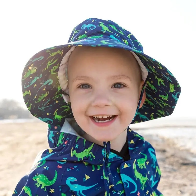 Jan & Jul Dinoland water-repellent bucket hat in blue with dinosaur print, worn by a smiling toddler.