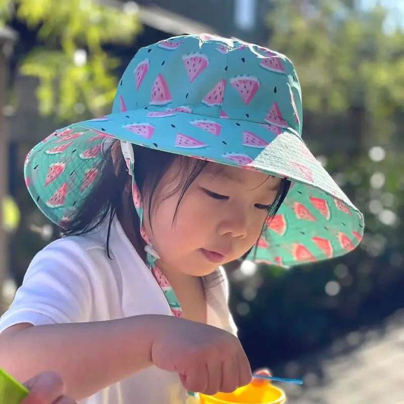Jan & Jul Kids Water Repellent Bucket Hats Watermelon in blue, child outdoors wearing a wide-brim hat with chin strap secured.