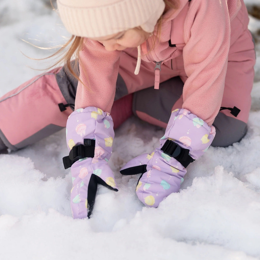 JAN & JUL Kids Waterproof Mittens Macarons in lavender, shown on a child pressing snow with strap-secured, waterproof mittens.
