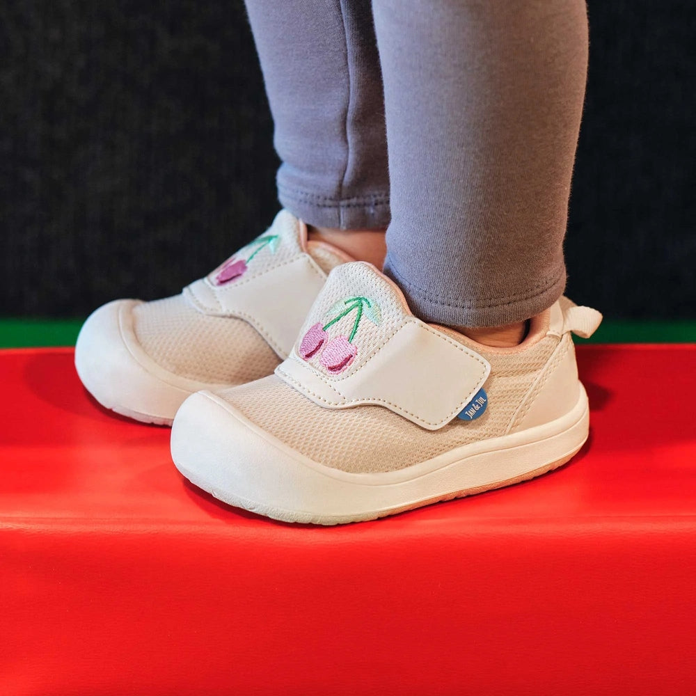 Jan & Jul Mini-Flyer Toddler Sneakers Cherries in beige mesh with white sole, cherry embroidery, worn by toddler.