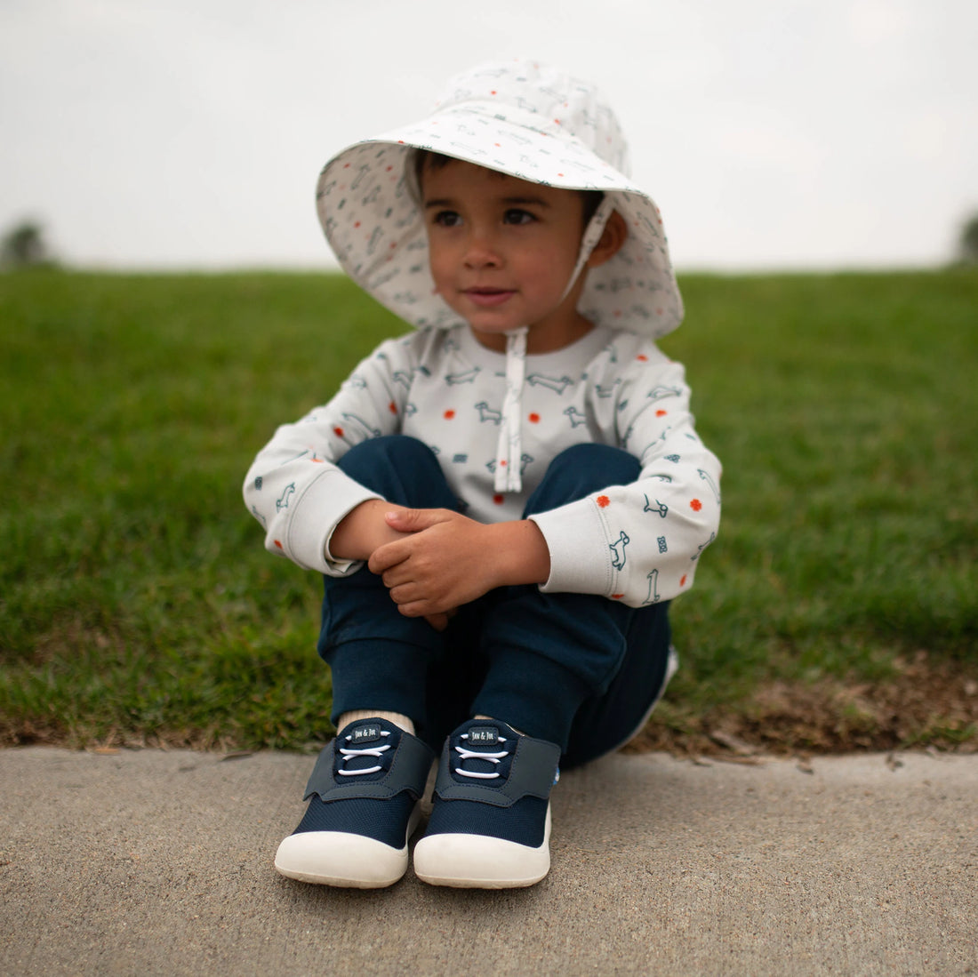 Toddler sitting outdoors wearing Jan & Jul Dark Navy Mini-Flyer sneakers.
