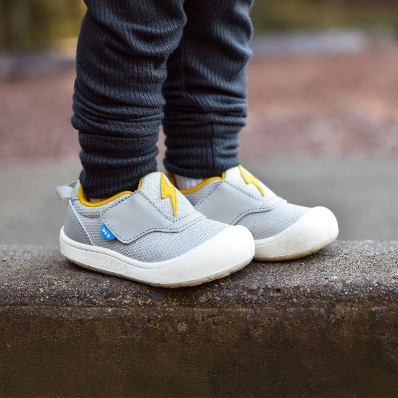 JAN & JUL Mini-Flyer Toddler Sneakers Lightning Bolt in gray with yellow bolts, shown on a child's feet.