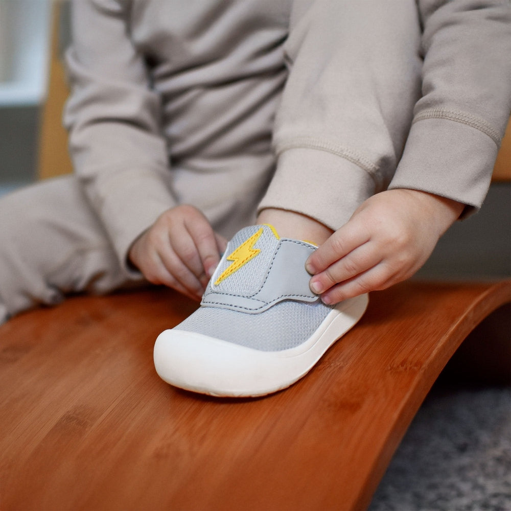 Jan & Jul Mini-Flyer Toddler Sneakers Lightning Bolt in light gray with yellow bolt, toddler fastens the strap.