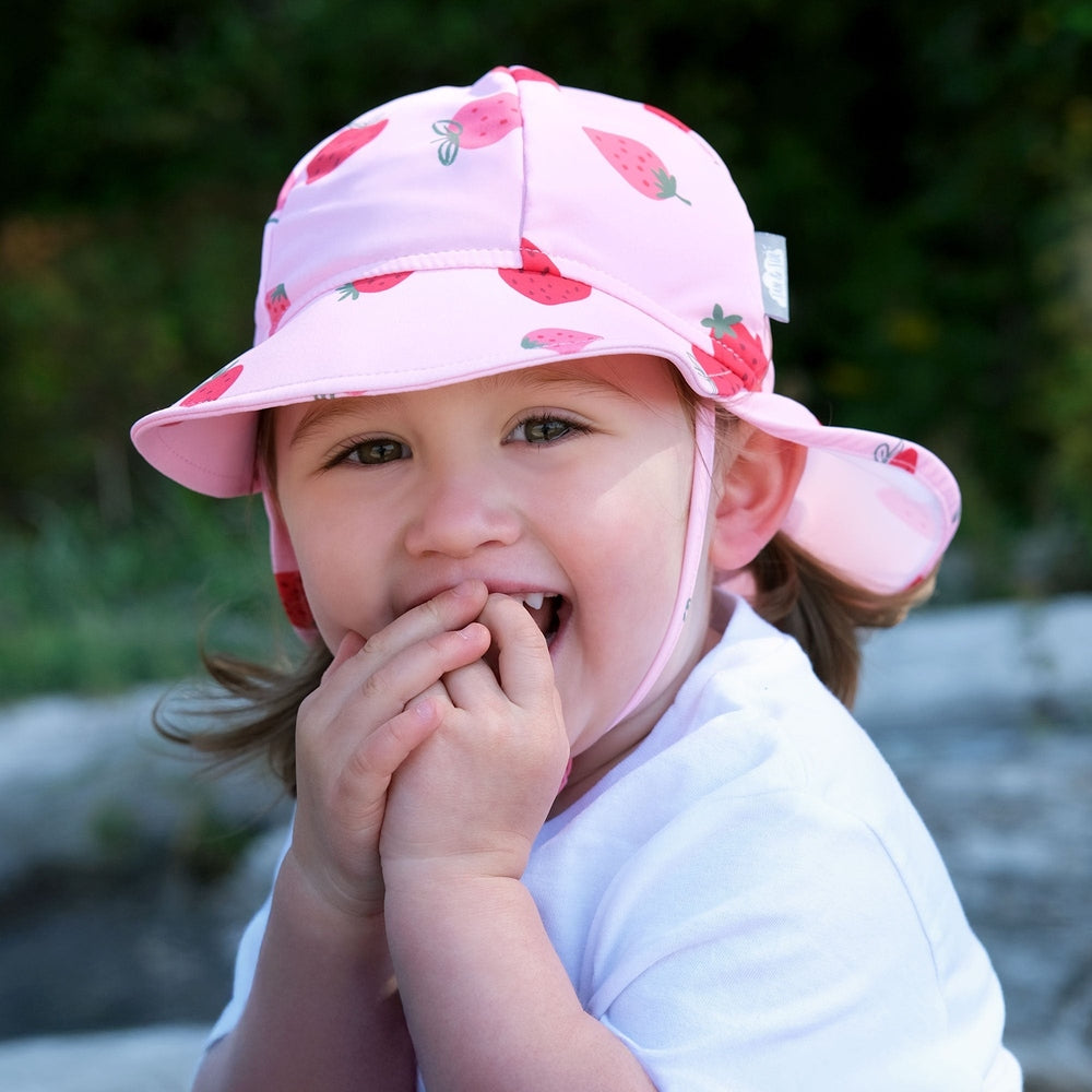 Jan & Jul Sun Soft UV Baby Cap Pink Strawberry, pink strawberry print sun hat with wide brim worn by a smiling toddler.