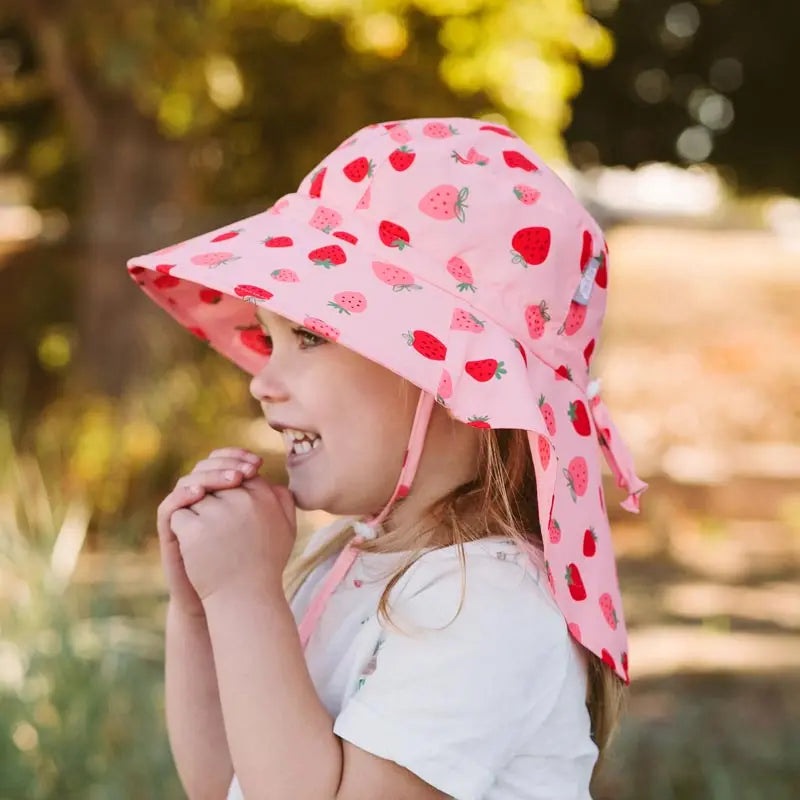 JAN & JUL Water Repellent Adventure Hat Pink Strawberry print, worn by a smiling child outdoors with an adjustable chin strap.
