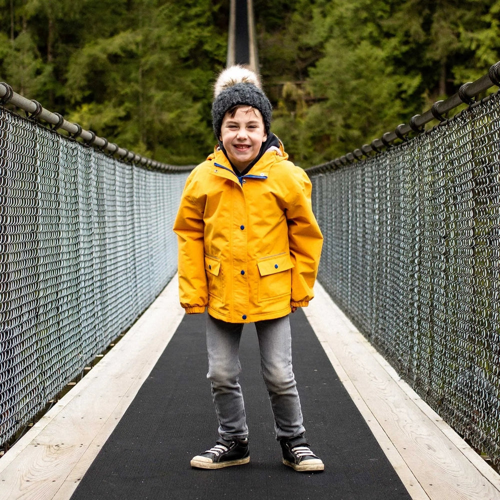 Jan & Jul Waterproof Cozy Dry Rain Jacket Yellow worn by a child on a bridge, showing front pockets.