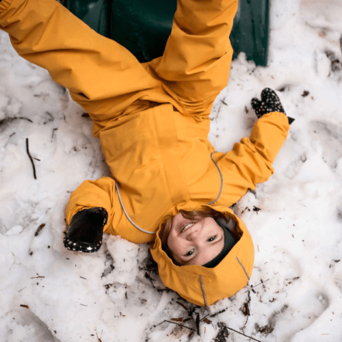 JAN & JUL Waterproof Cozy Dry Rain Suit Yellow; child playing in snow, lying on back in bright hooded waterproof outerwear.