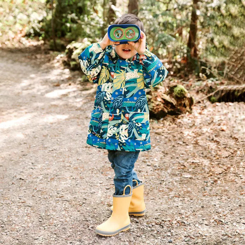 JAN & JUL Waterproof Puddle Dry Rain Jacket Jungle Nights worn by a child walking a forest path in yellow rain boots