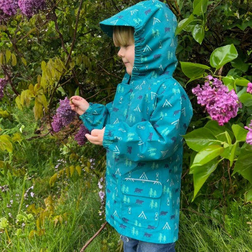 JAN & JUL Waterproof Puddle Dry Rain Jacket Summer Camp; child outdoors in teal hooded jacket, touching flowers.