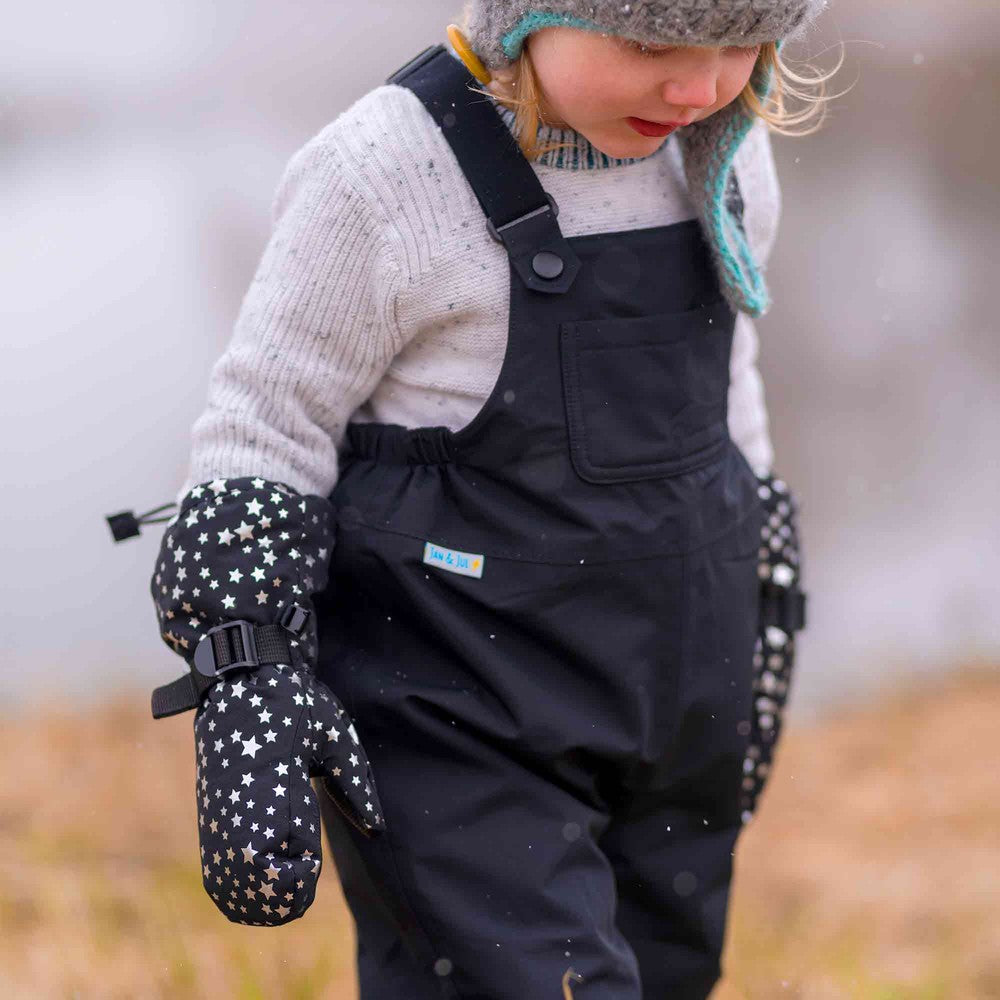 Jan & Jul Waterproof Toasty Dry Mitten Black Star worn by a toddler, star-pattern gloves strapped for a snowy outdoor walk.
