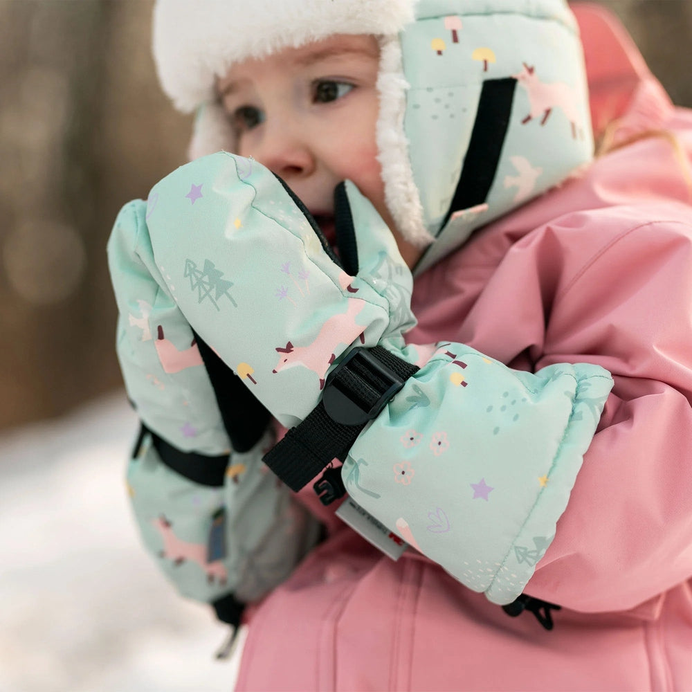 Toddler wearing JAN & JUL Waterproof Toasty Dry Mitten Minty Forest mittens on a pink winter jacket in a snowy outdoor scene.