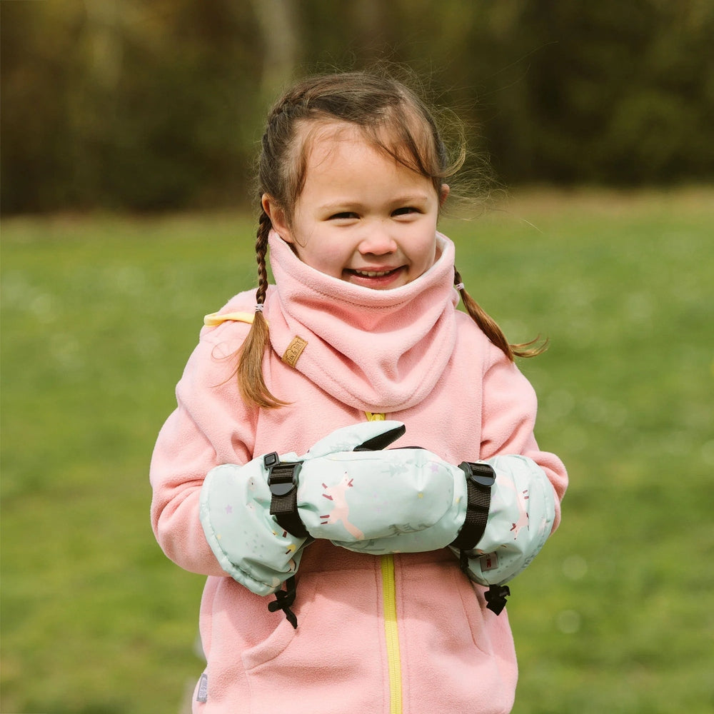 JAN & JUL Waterproof Toasty Dry Mitten Minty Forest on a smiling toddler wearing a pink fleece jacket, hands clasped outdoors
