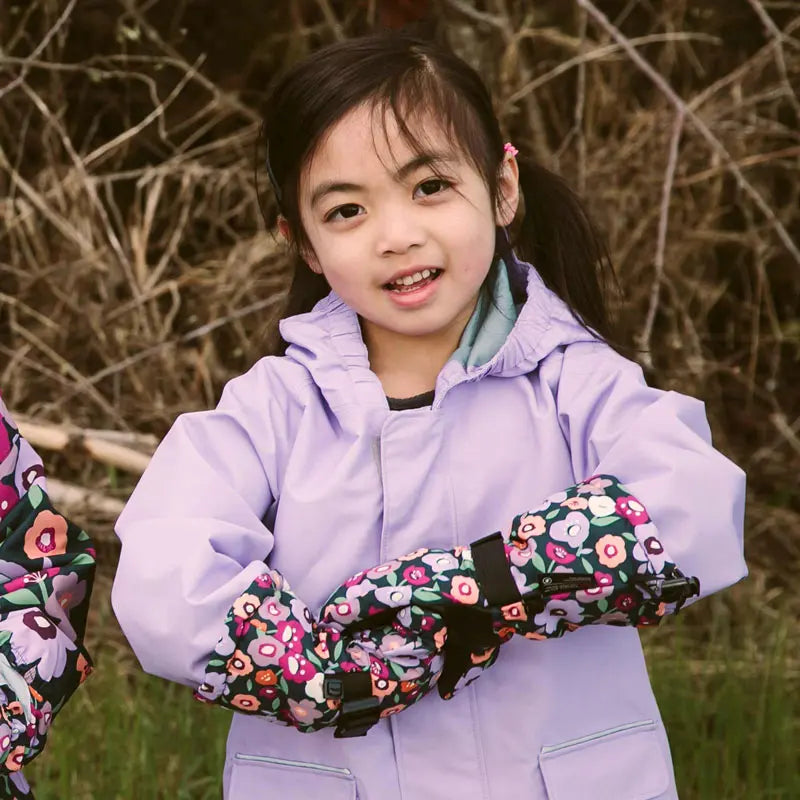 JAN & JUL Waterproof Toasty Dry Mittens Winter Flowers worn by a girl in a lavender jacket, floral-pattern mittens with straps