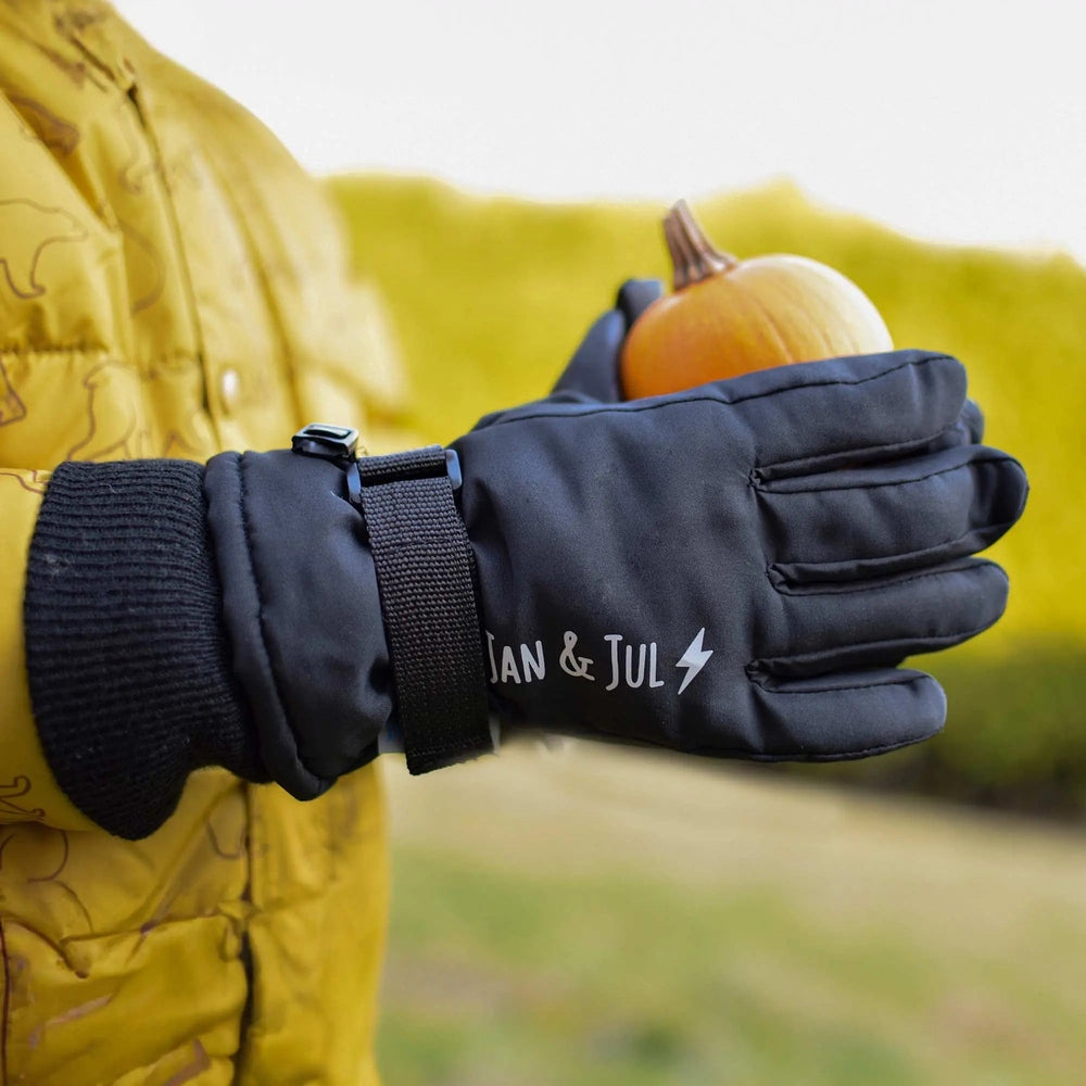 Jan & Jul Waterproof Toasty Dry Snow Gloves Black; child grips a pumpkin outdoors, showing secure strap.