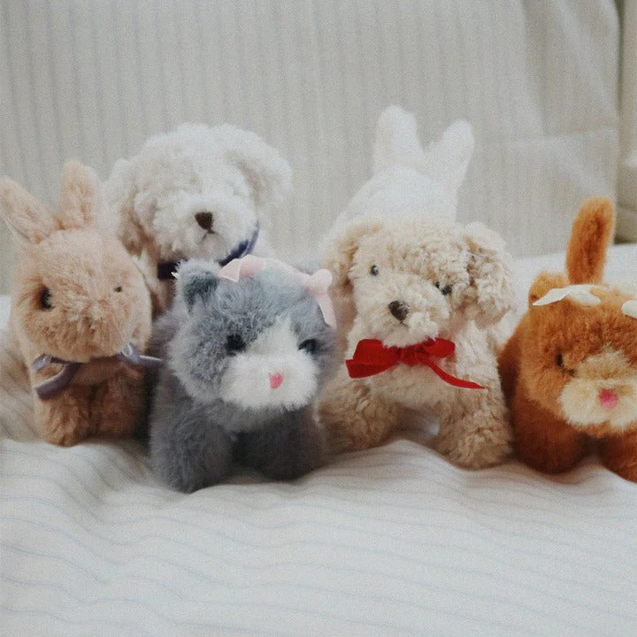Konges Slojd Baby Animals plush toy set-five soft bunnies and cats with ribbons, lined up on a striped bed.