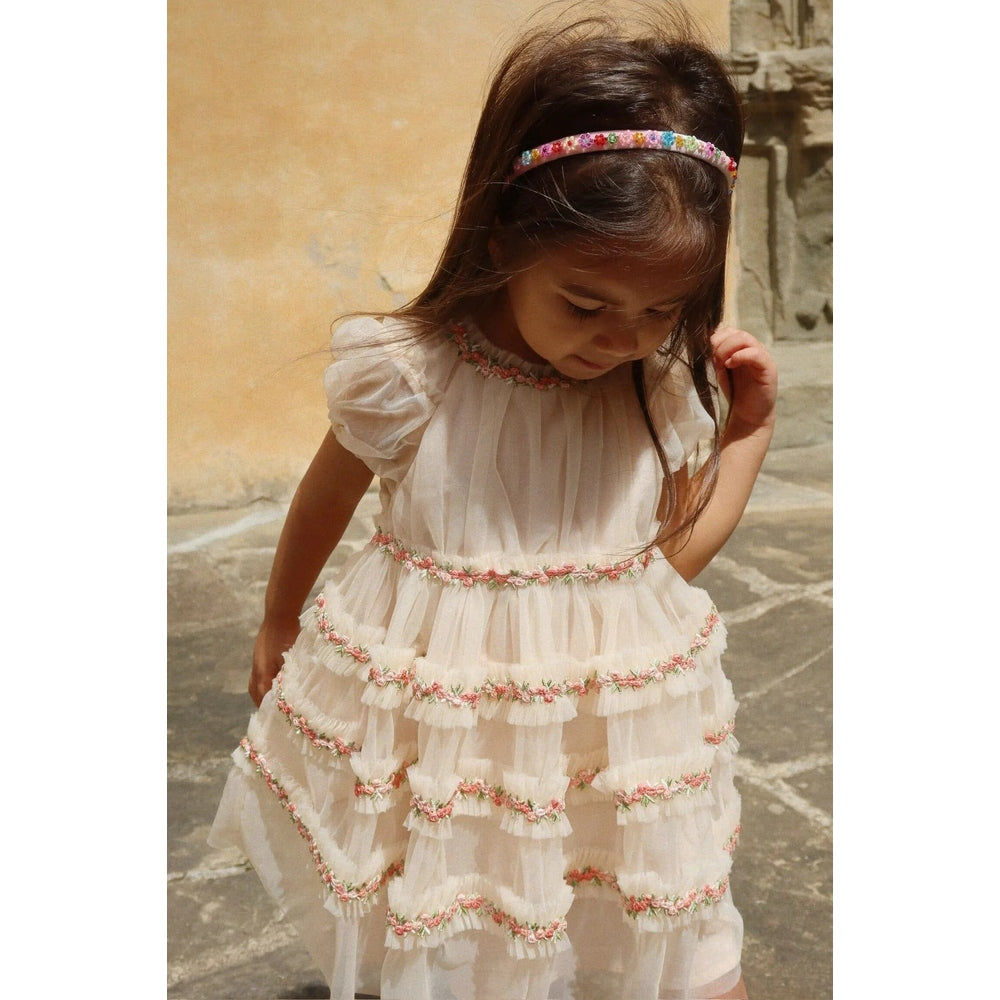 Konges Slojd Joelle Dress in Buttercream, cream tiered dress with pink floral trim and ruffles; girl with beaded headband.