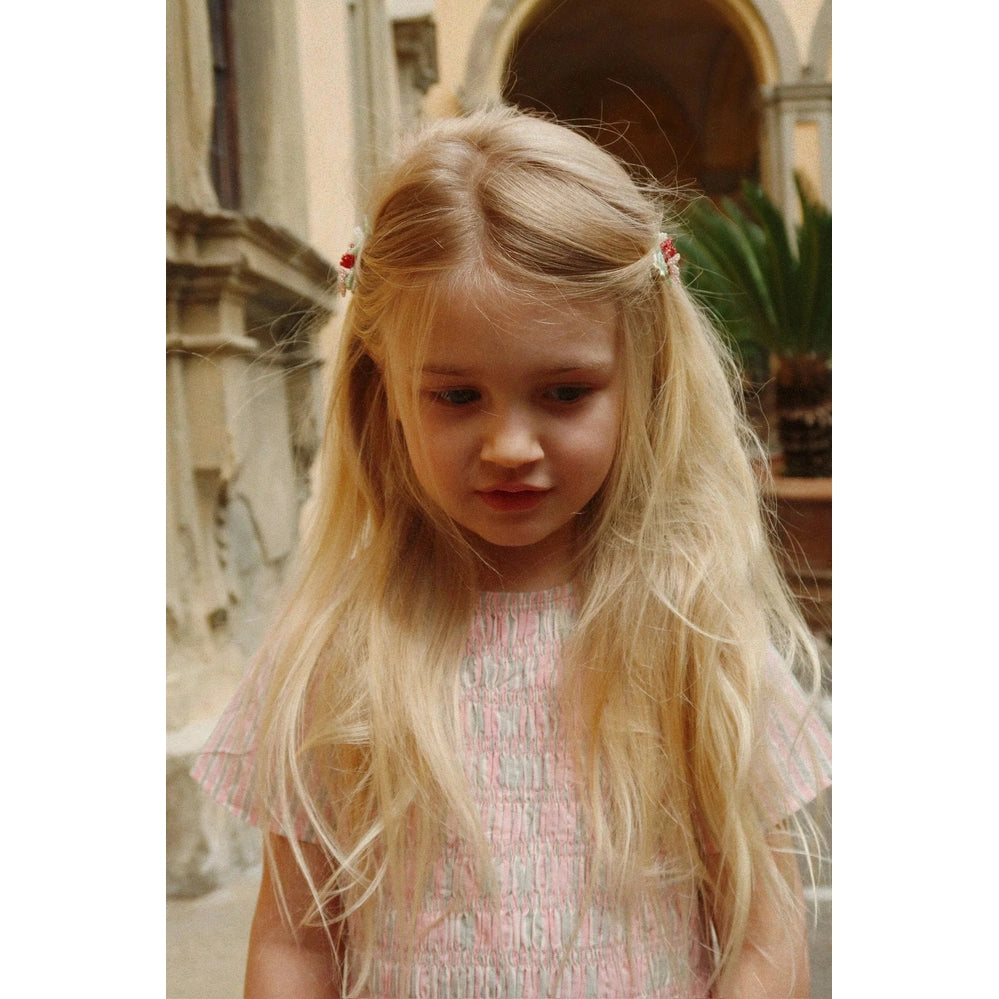 Konges Slojd Luli Dress in Blush Stripe on a blonde-haired girl with red hair clips outdoors
