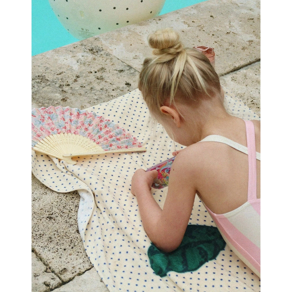 Konges Slojd Water Ring Toss Game in poolside scene with turquoise pool water, a girl in a pink swimsuit on a dotted towel.
