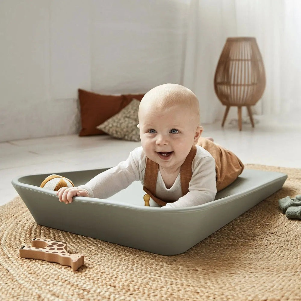 Leander Matty Changer in gray, cheerful baby reaching forward on the tray in a bright room.