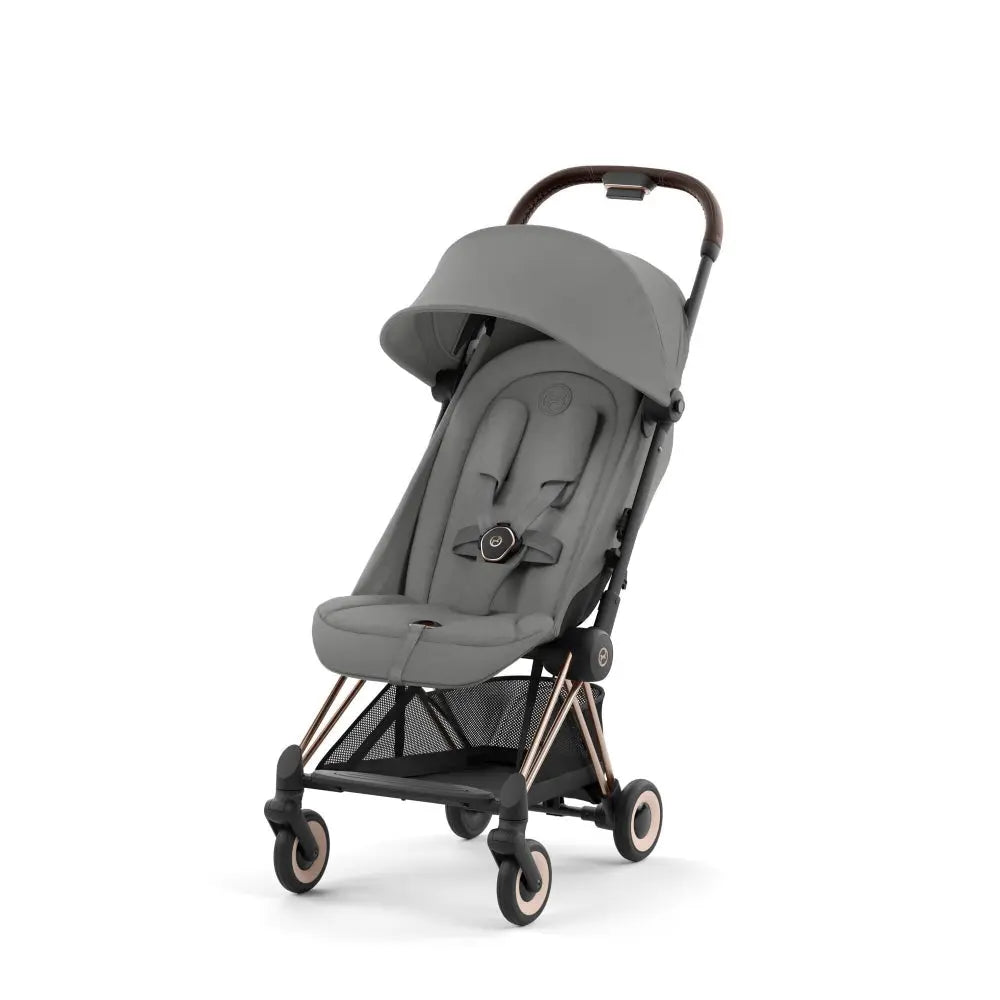 Lifestyle image of the Cybex Coya Rose Gold Frame Stroller in grey with canopy deployed and storage basket visible.