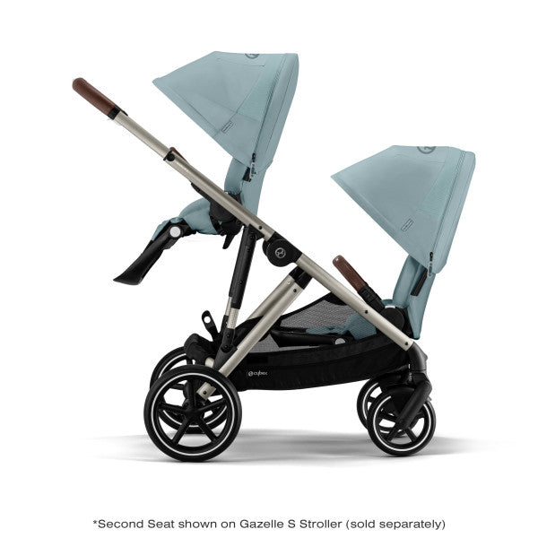 Lifestyle image of the Cybex Gazelle S V2 Toddle Seat twin-stroller in light teal with brown grips, dual seats and extended canopies.
