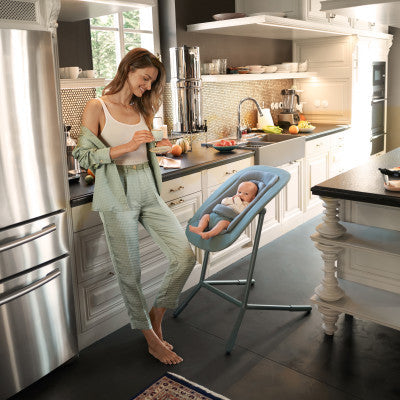 Lifestyle image of the Cybex Lemo 2 Bouncer woman in a kitchen with a baby in a high chair, surrounded by modern appliances and decor.
