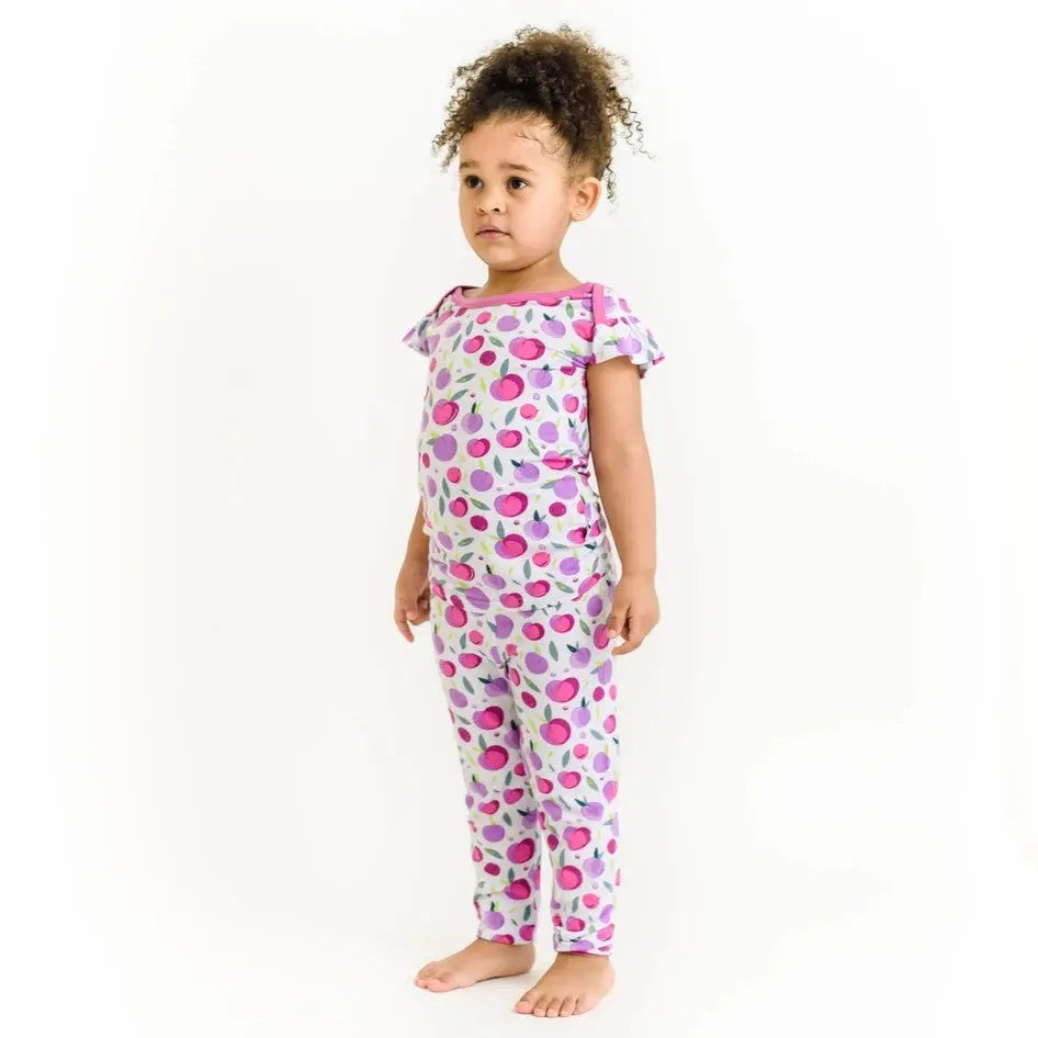 Little Sleepies Bamboo Pajama Set Plum worn by a toddler standing, pink-purple fruit print highlights soft bamboo fabric.