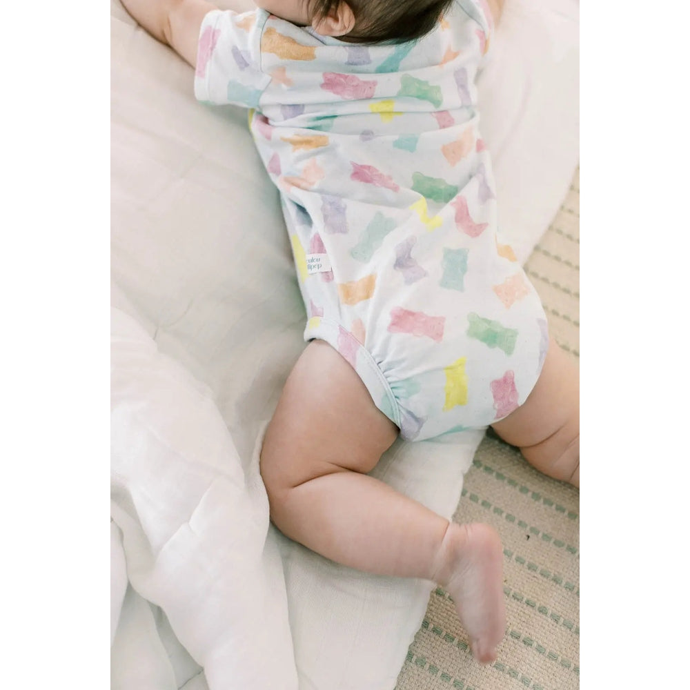 Loulou Lollipop Gummy Bears baby bodysuit in pastel print on soft cotton, as baby crawls on a bed.