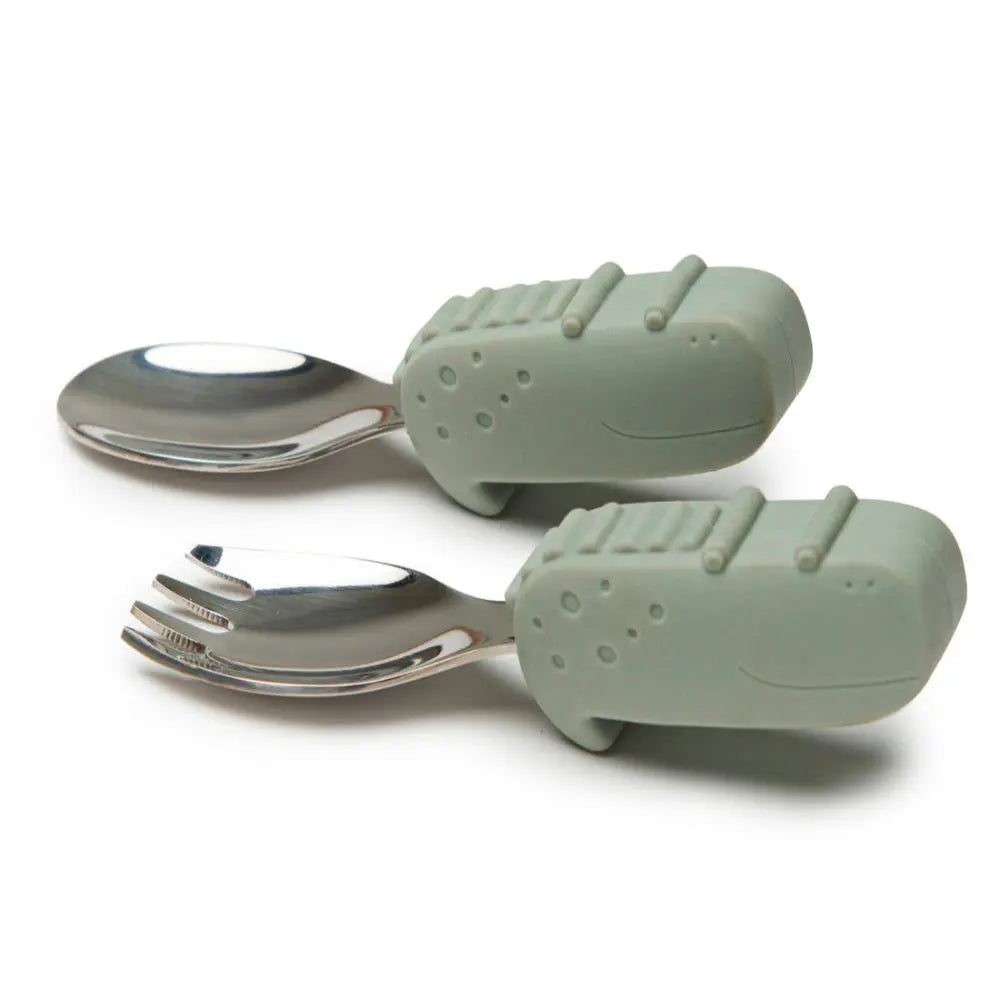 LOULOU LOLLIPOP Born To Be Wild Learning Spoon/Fork Set with green dinosaur silicone covers, two utensils laid ready for feeding.