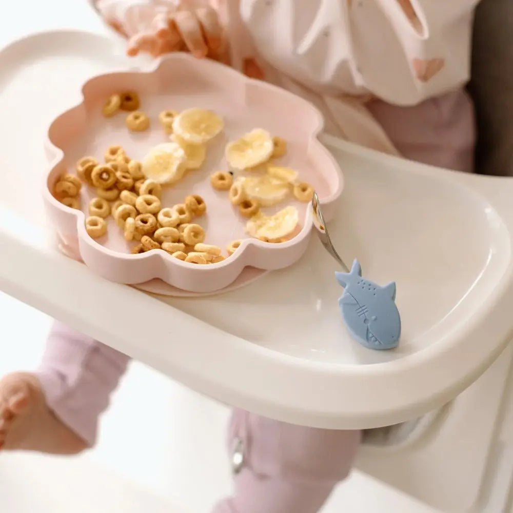 Loulou Lollipop Born To Be Wild Silicone Snack Plate in pink, cereal and banana pieces, with a blue shark spoon scooping bites.