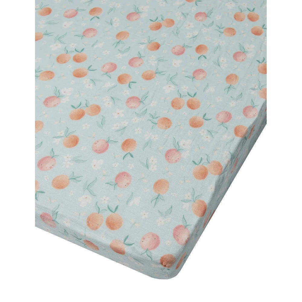 Loulou Lollipop Fitted Crib Sheet in light blue with peach-orange fruit pattern, securely fitted to the mattress.