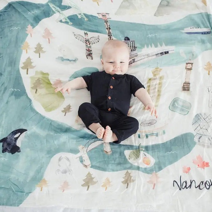 Loulou Lollipop Muslin Quilt Blanket in teal map design; baby lies comfortably on soft, breathable fabric.