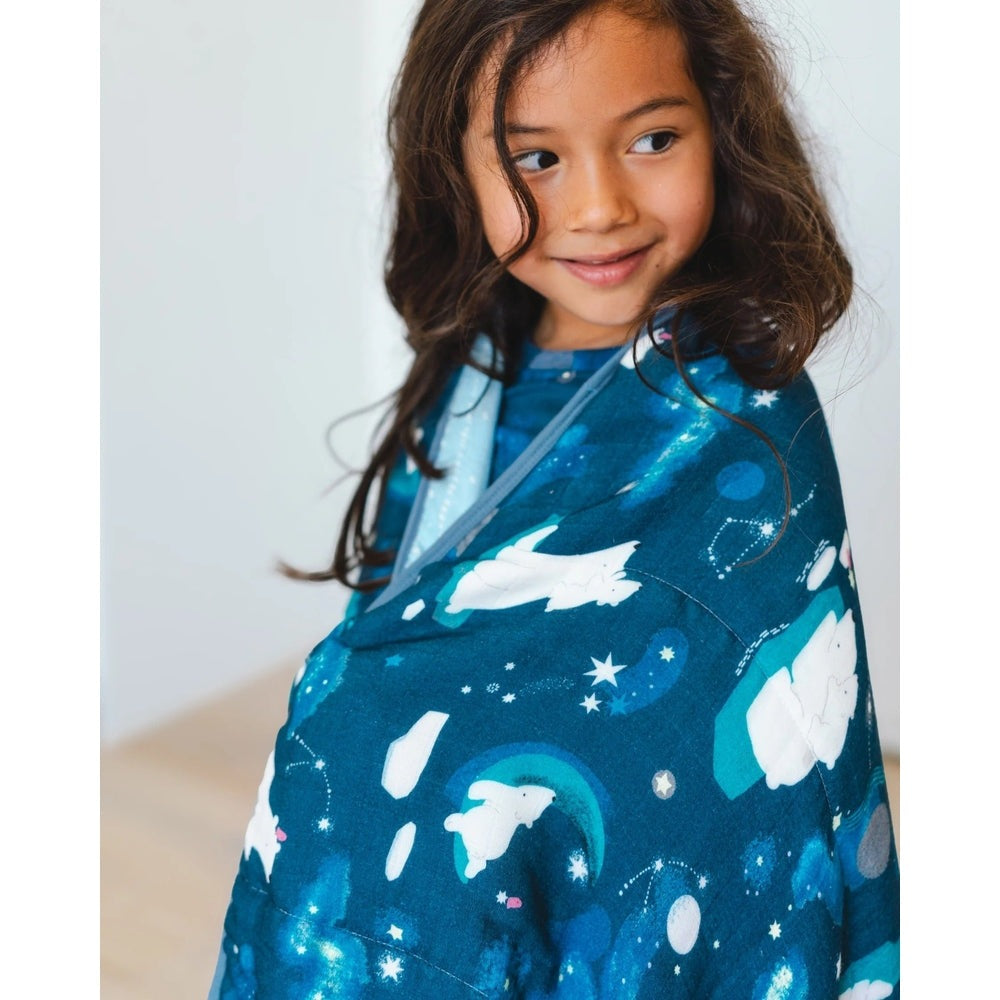 Loulou Lollipop Muslin Quilt Blanket in blue space print draped over a smiling girl, acting as a cozy swaddle.