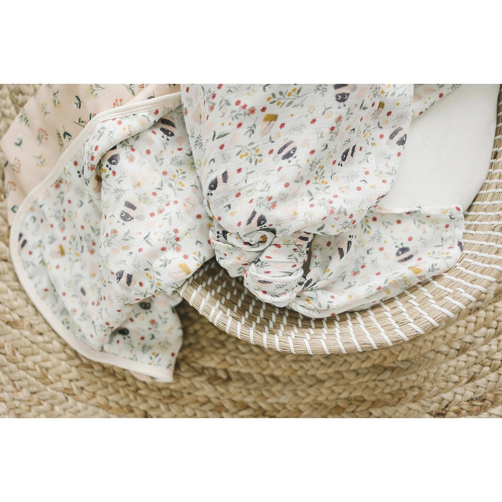 Loulou Lollipop Muslin Quilt Blanket in soft floral print folded in a woven basket for cozy baby swaddling.