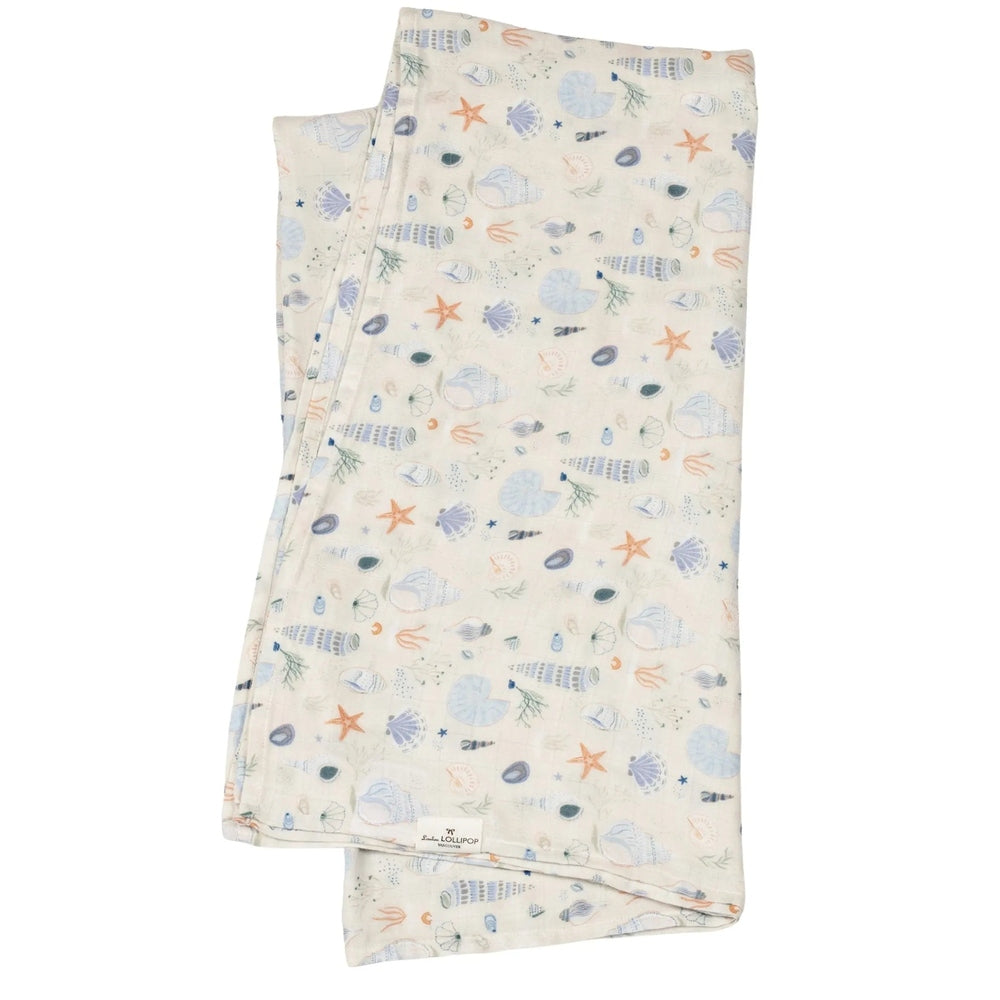 LOULOU LOLLIPOP Muslin Swaddle blanket in cream with pastel seashells and starfish, gently folded to show breathable fabric.