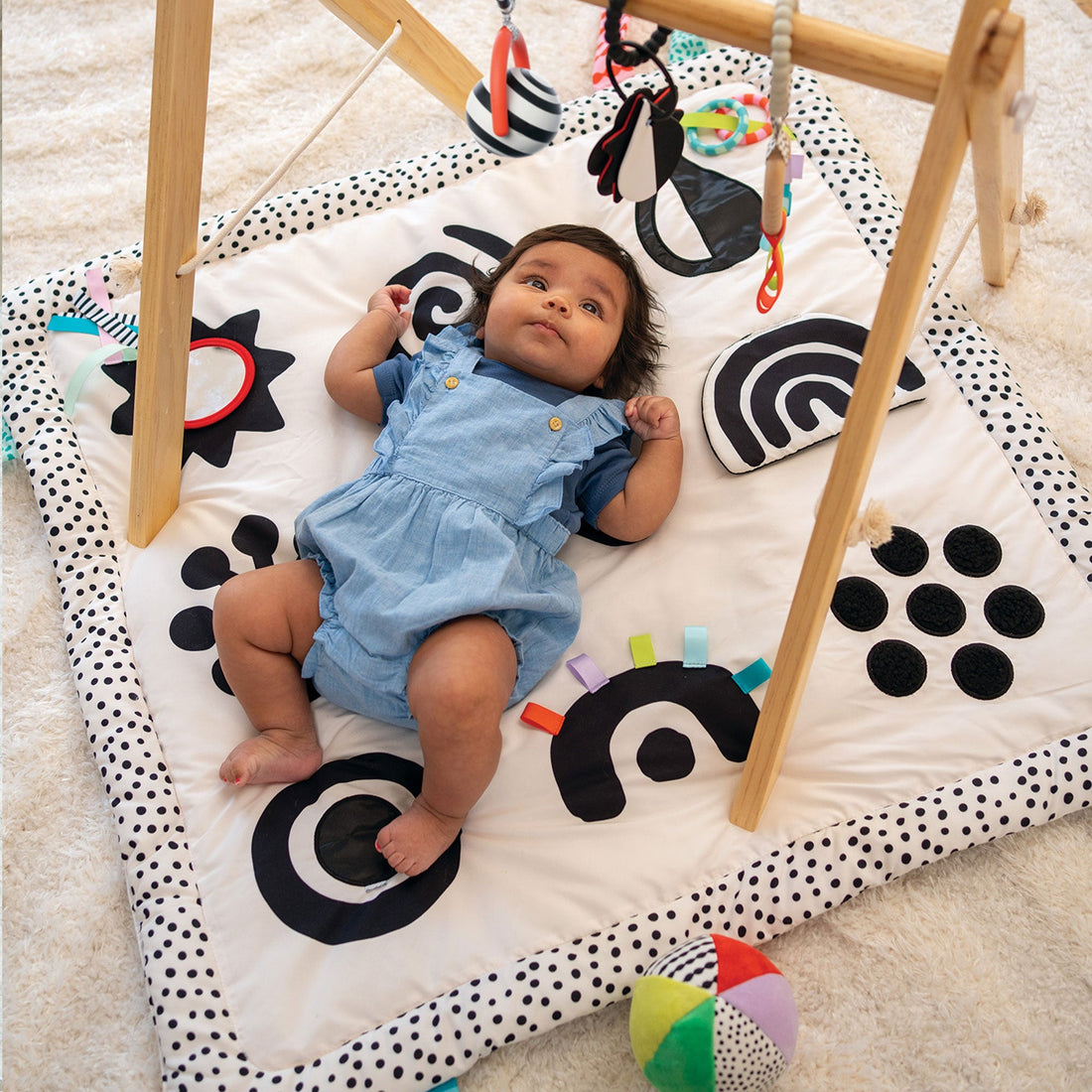 Manhattan Toy Wimmer Seek & Explore Mat - baby lying on the graphic mat beneath a play gym