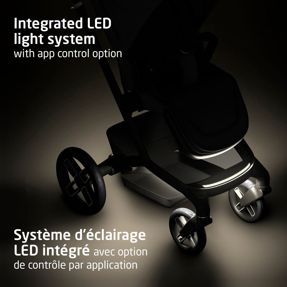 Black stroller with LED light strip along the base, metal frame and dark fabric seat, three visible wheels.