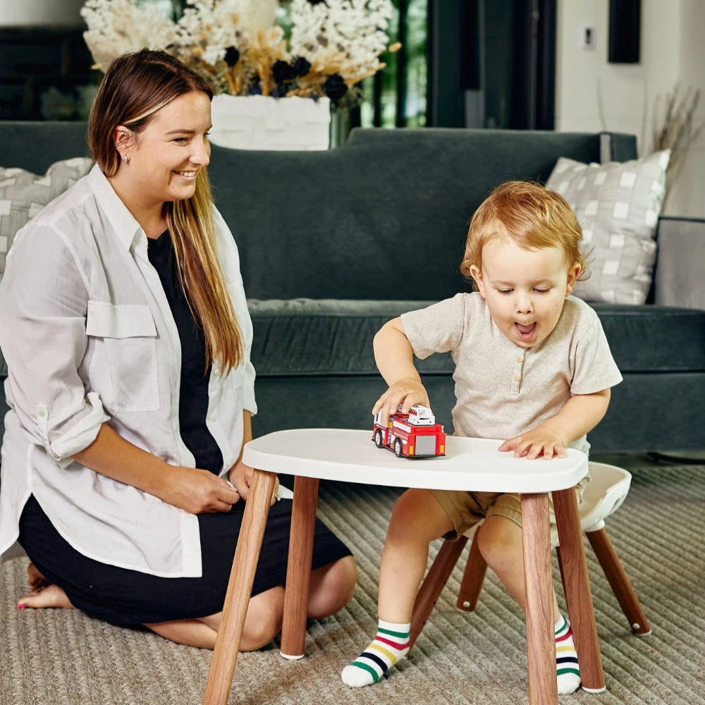 Maxi Cosi Moa 8-in-1 high chair with white tray and natural wood legs; toddler plays with a toy fire truck nearby.