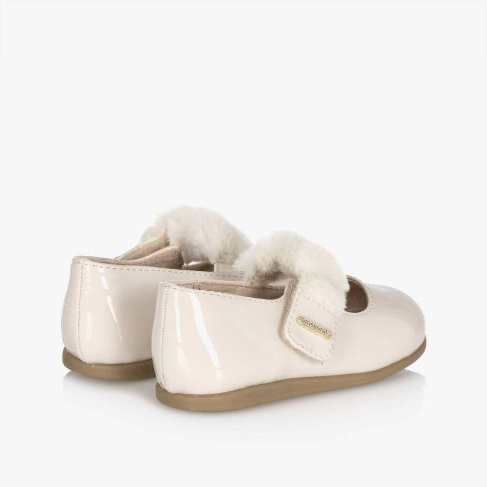 Mayoral Girl Patent Leather Mary Janes in cream with fluffy lining, Velcro straps fastened on a toddler's feet.
