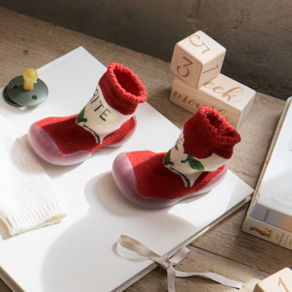 Mayoral newborn baby slipper socks in red with cream cuff and leaf design, resting on a white surface beside wooden blocks.