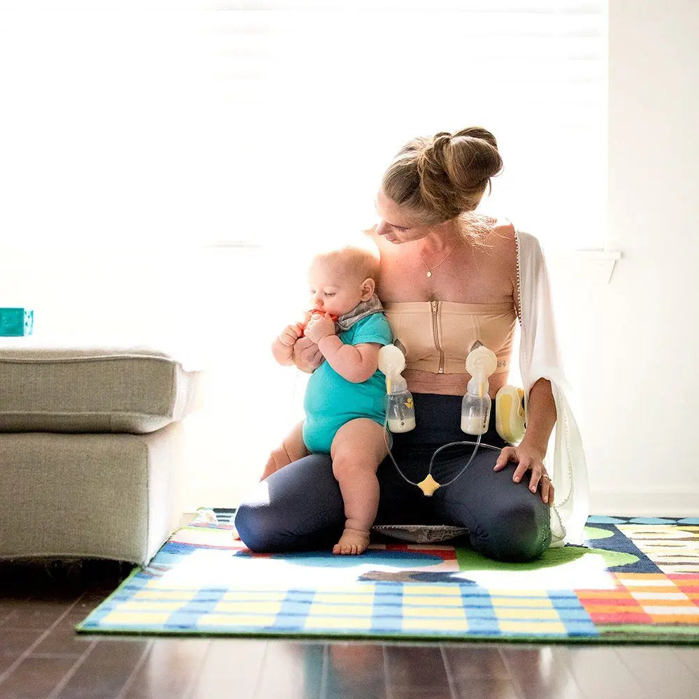 MEDELA Easy Expression Bustier Nude worn by a mom pumping hands-free with attached bottles while baby sits on her lap