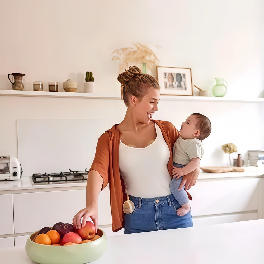 Medela Magic InBra Wearable Breast Pump: mom in a bright kitchen with her baby, fruit bowl nearby, showcasing comfort and ease.