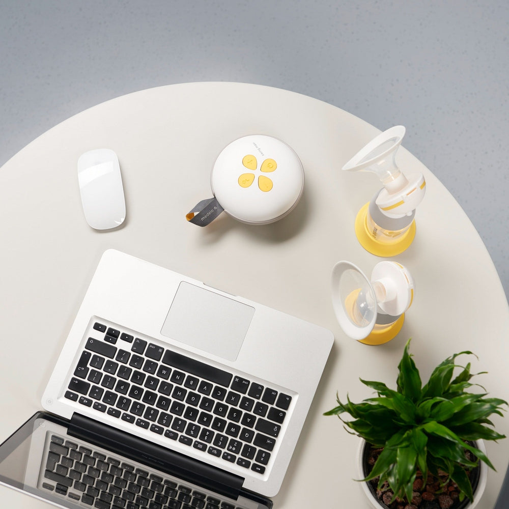 MEDELA Swing Maxi double electric breast pump with yellow bottle parts on round table beside a laptop