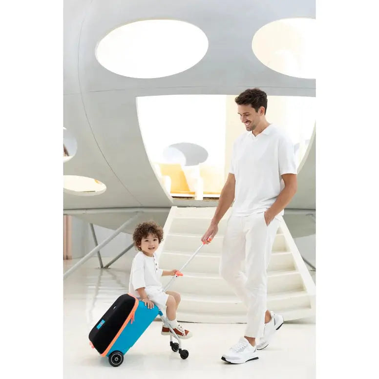 Micro Eazy Luggage kid-sized blue suitcase with black lid and orange accents, pulled by an adult as a child sits on it.