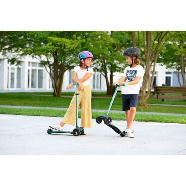 Micro Maxi Deluxe Eco Scooter Mint; two kids ride mint and green scooters wearing helmets in a sunny park.