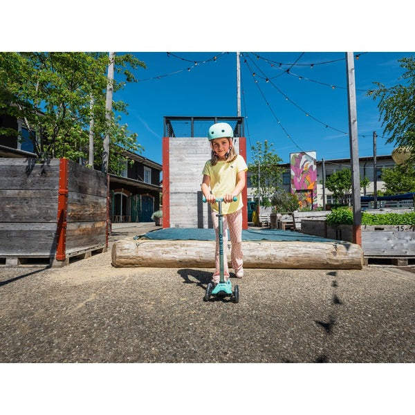 Micro Maxi Deluxe Eco Scooter Mint being ridden by a girl in a helmet on a sunny outdoor playground.