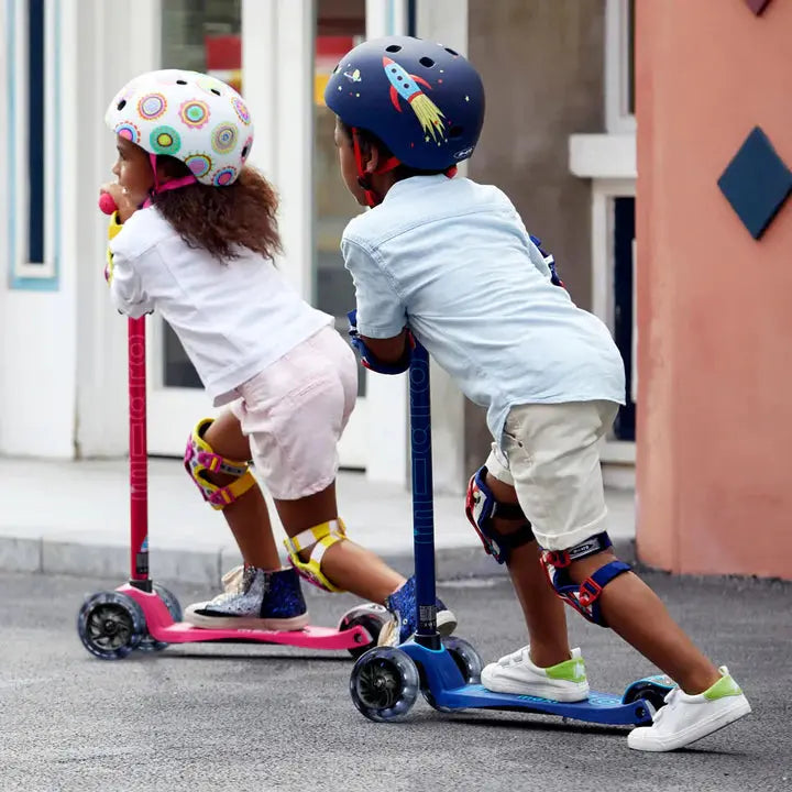 Micro Maxi Deluxe Led Scooter; two kids ride pink and blue scooters wearing helmets outdoors.