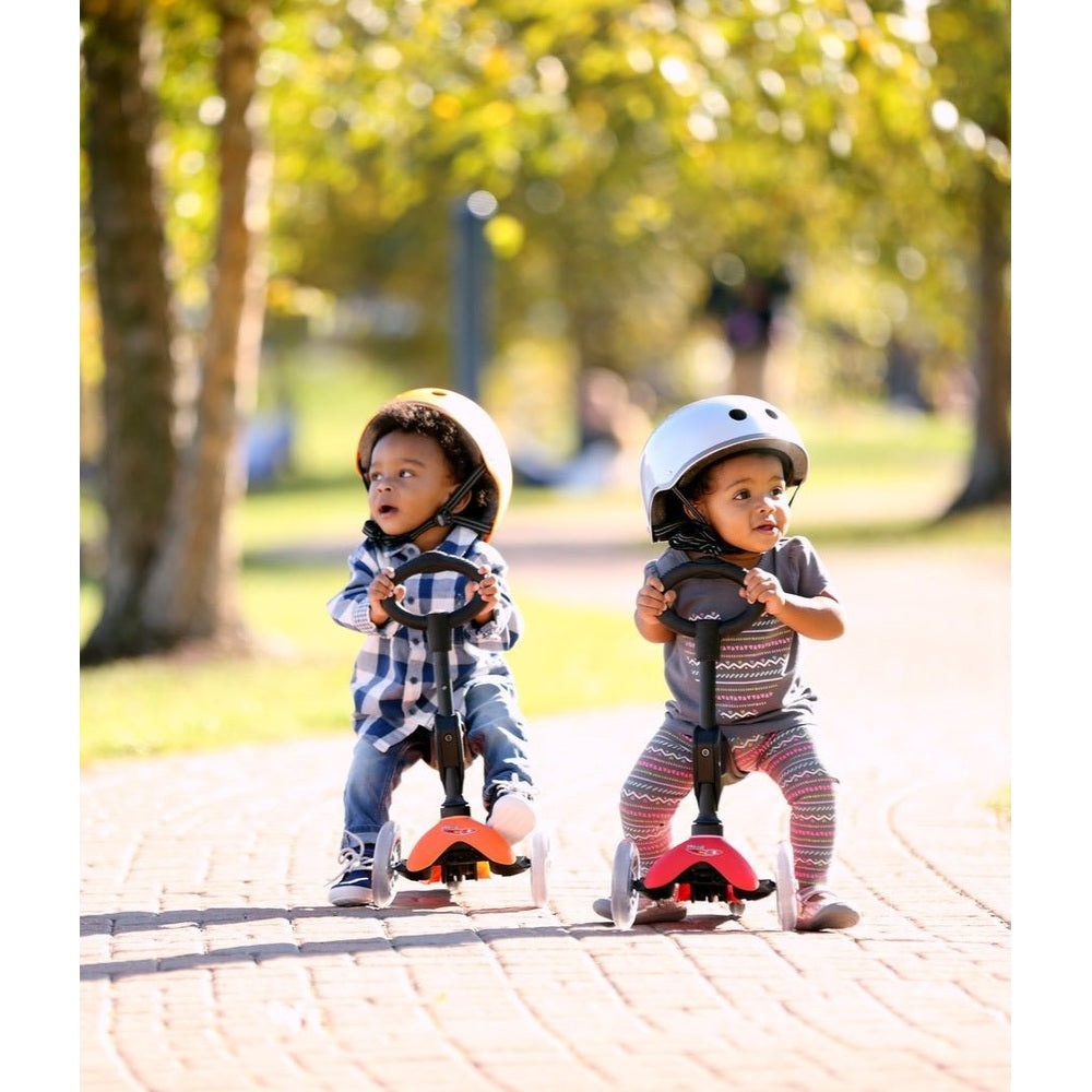 Micro Mini 3In1 Deluxe Scooter Pink; two toddlers ride pink MICRO scooters in helmets along a sunny park path