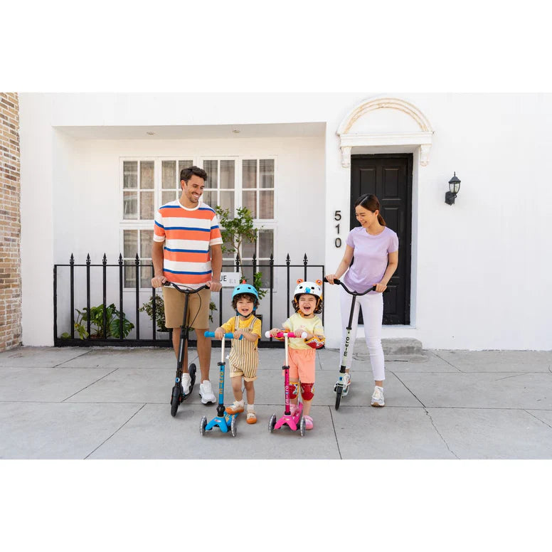 MICRO Micro Mini Deluxe Foldable Scooter; outdoors with four colorful scooters as parents guide two kids on their bikes/scooters.
